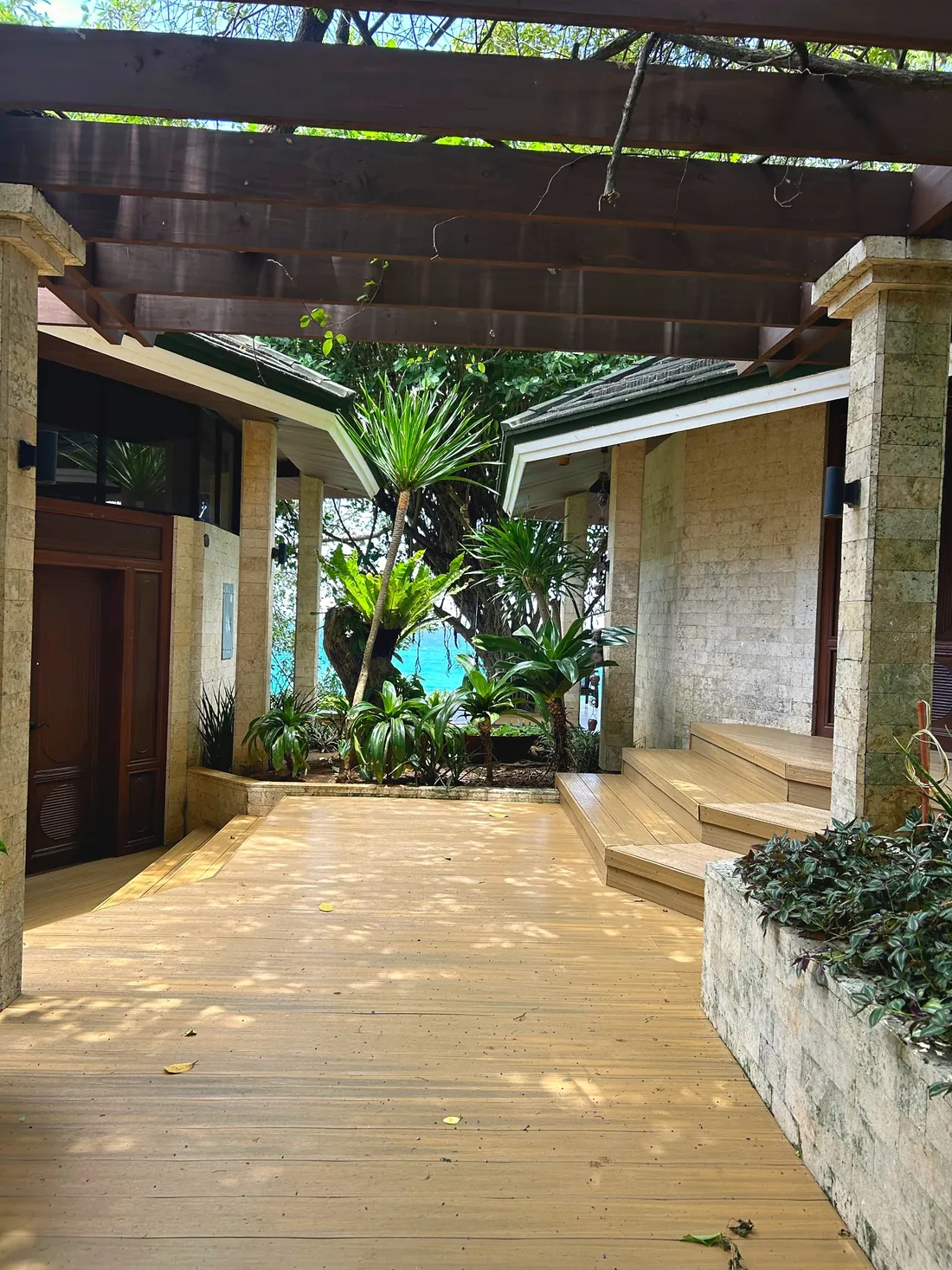 Stone courtyard under a timber pergola, with a glimpse of the sea