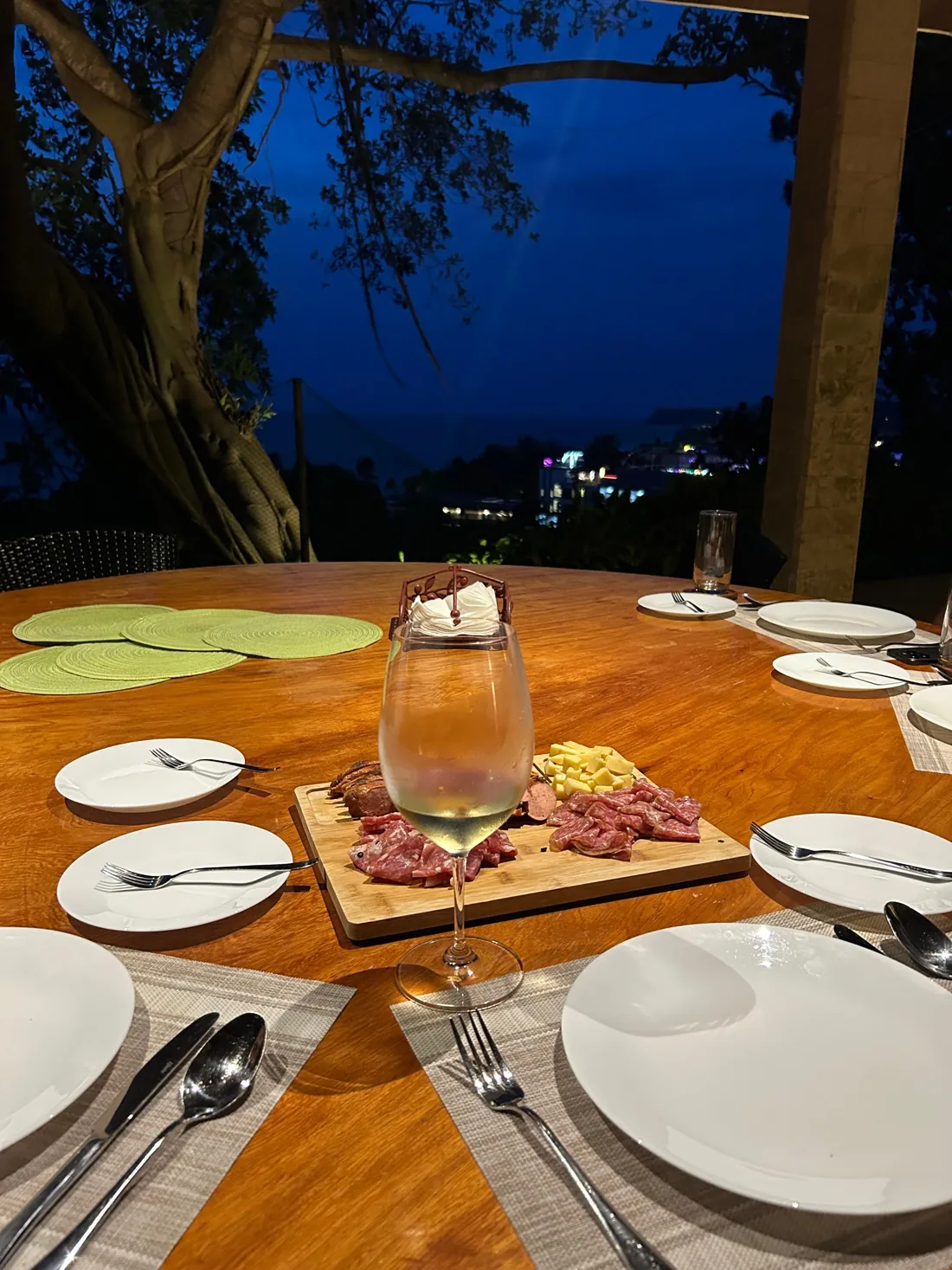 Table set for dinner at dusk, with the lights of the coast below